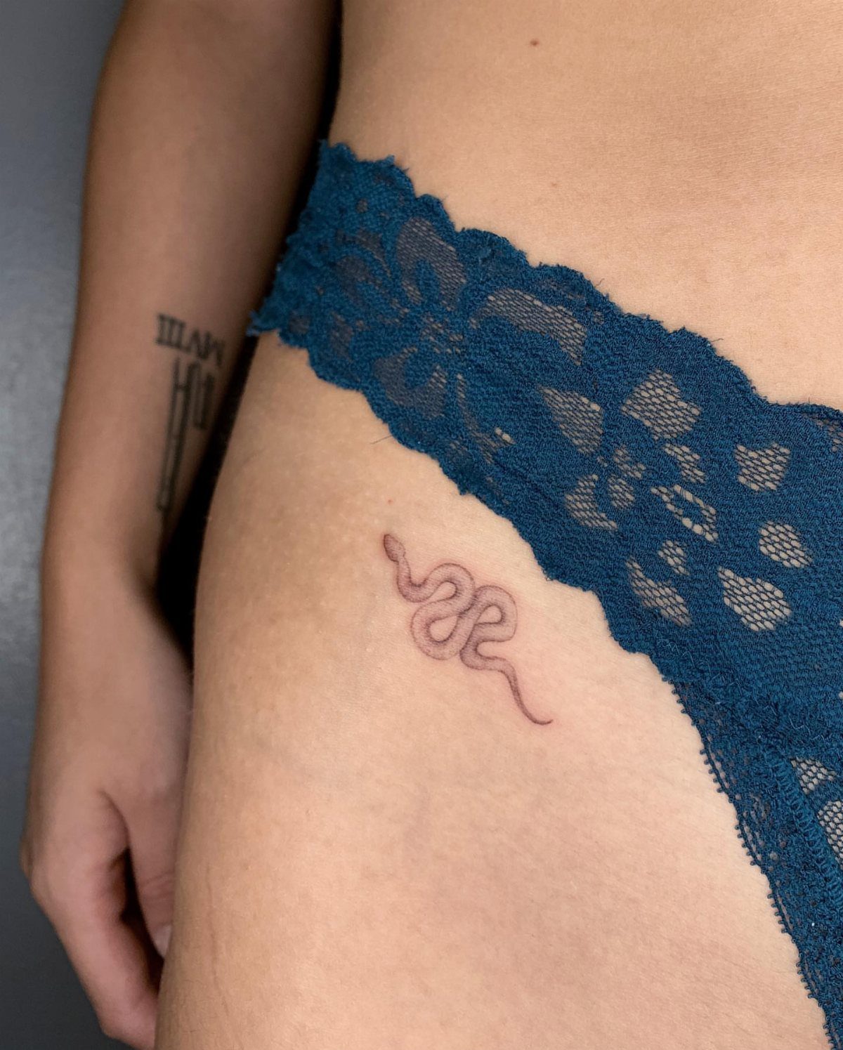 A small minimalist snake tattoo located on a person's hip near blue lace underwear.