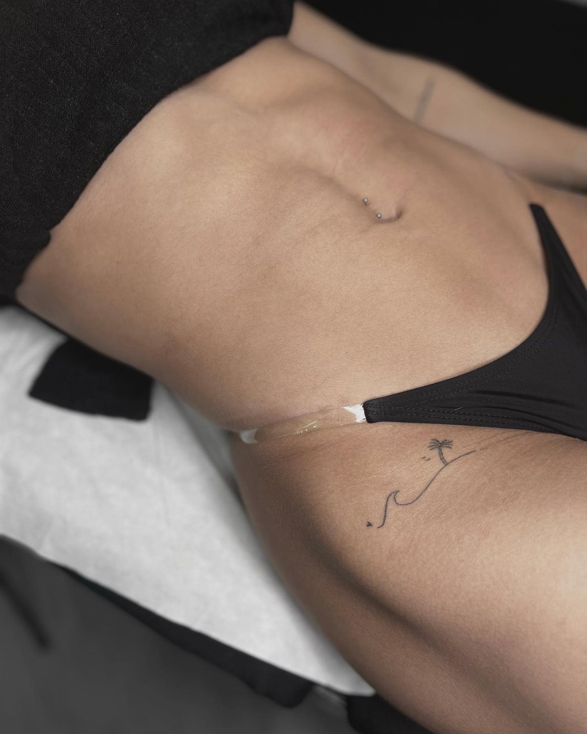 A small minimalist tattoo of a wave and palm tree on a person's hip.