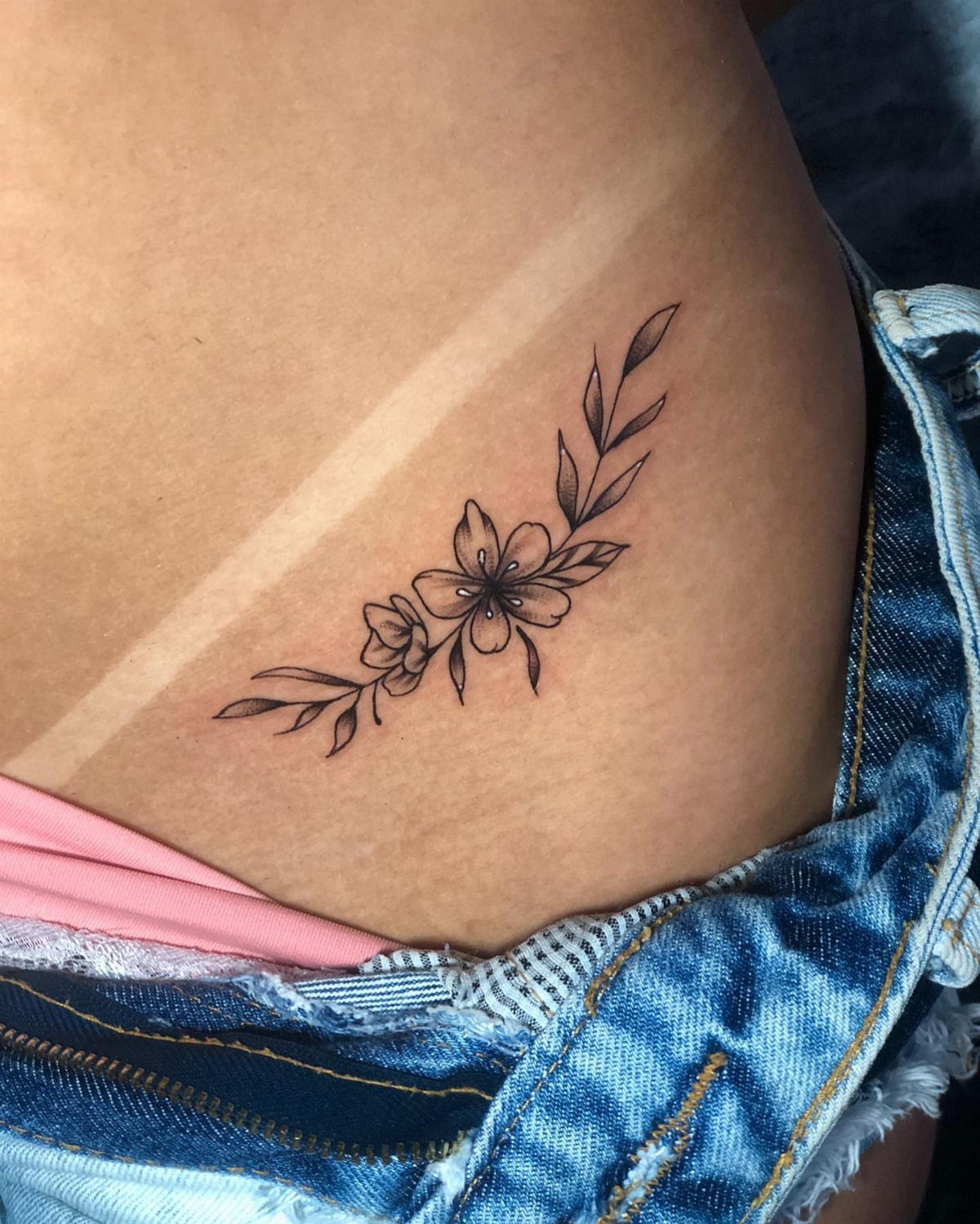 15 Small Tattoo Placement Ideas for Every Style 14 A black ink floral tattoo on a person's hip near blue denim shorts.
