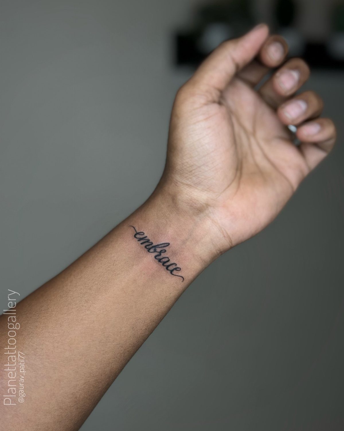 15 Small Tattoo Placement Ideas for Every Style 1 A small black cursive tattoo reading embrace on a person's inner wrist.