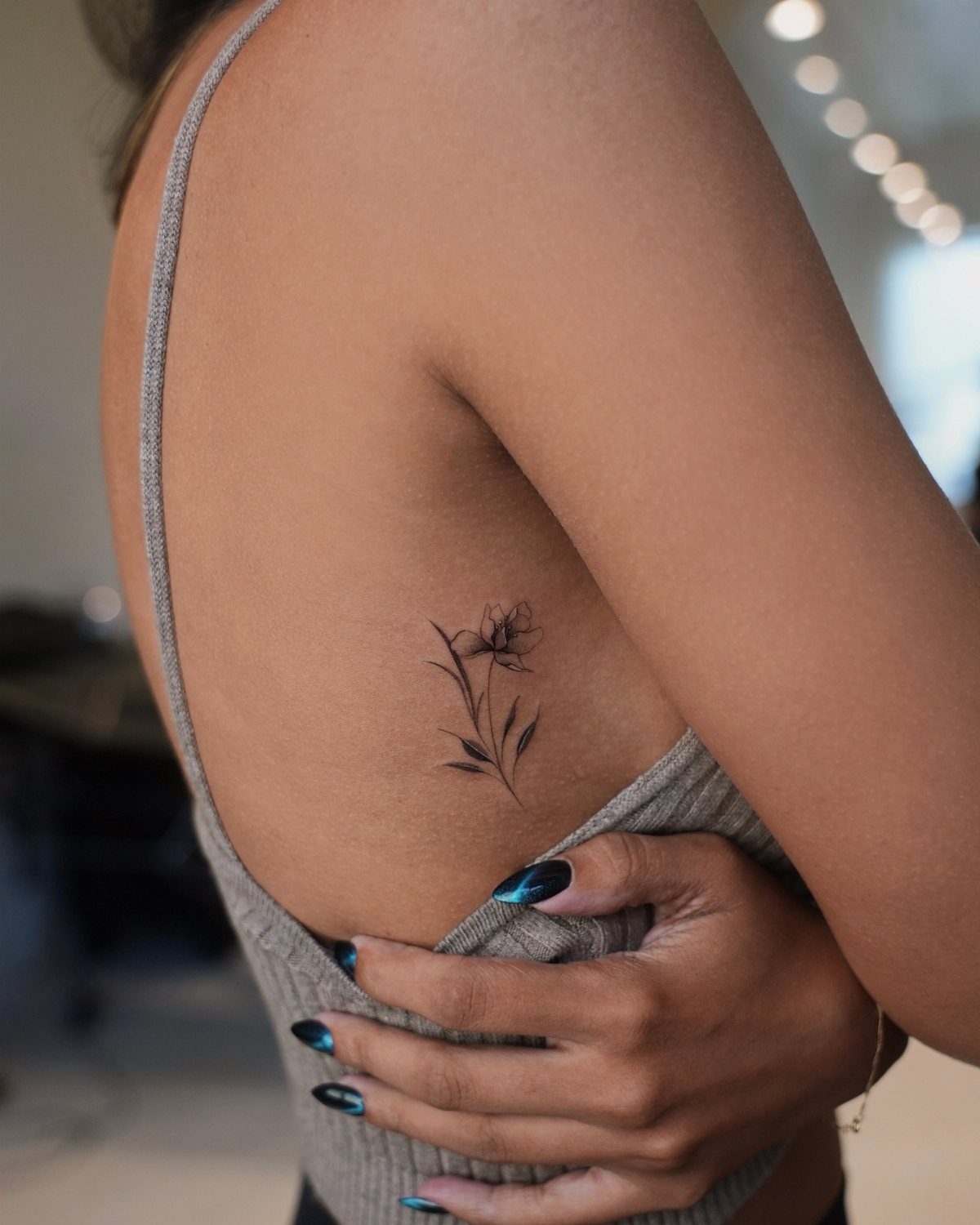 15 Small Tattoo Placement Ideas for Every Style 8 A fine-line floral tattoo on a person's ribcage near their grey tank top.