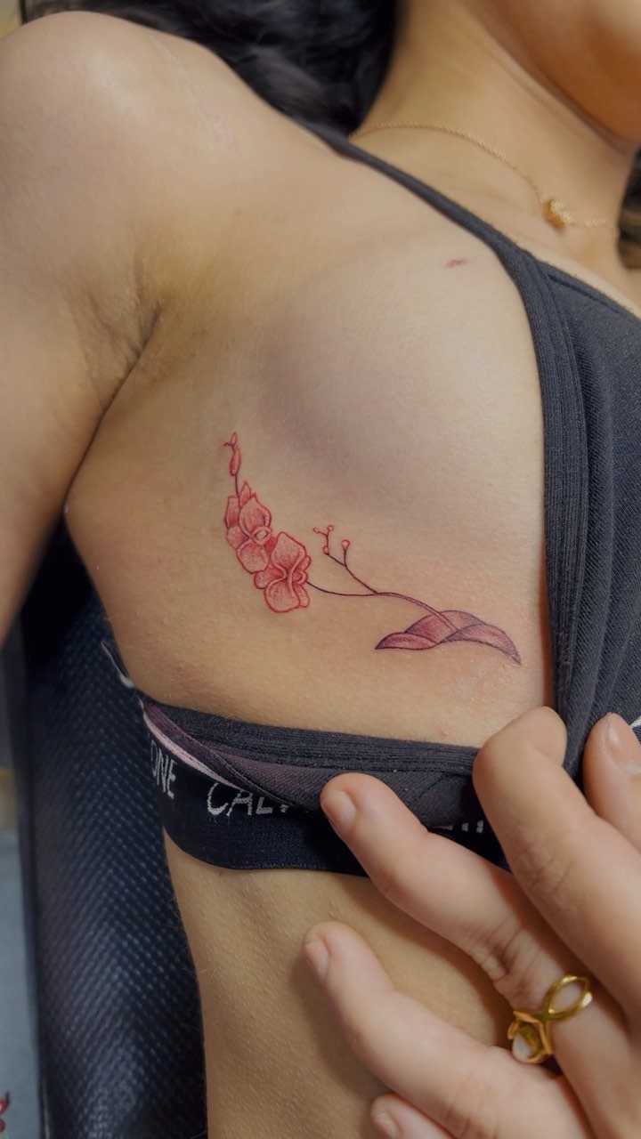 15 Small Tattoo Placement Ideas for Every Style 9 A red orchid tattoo placed on a person's ribcage below the side of the breast.