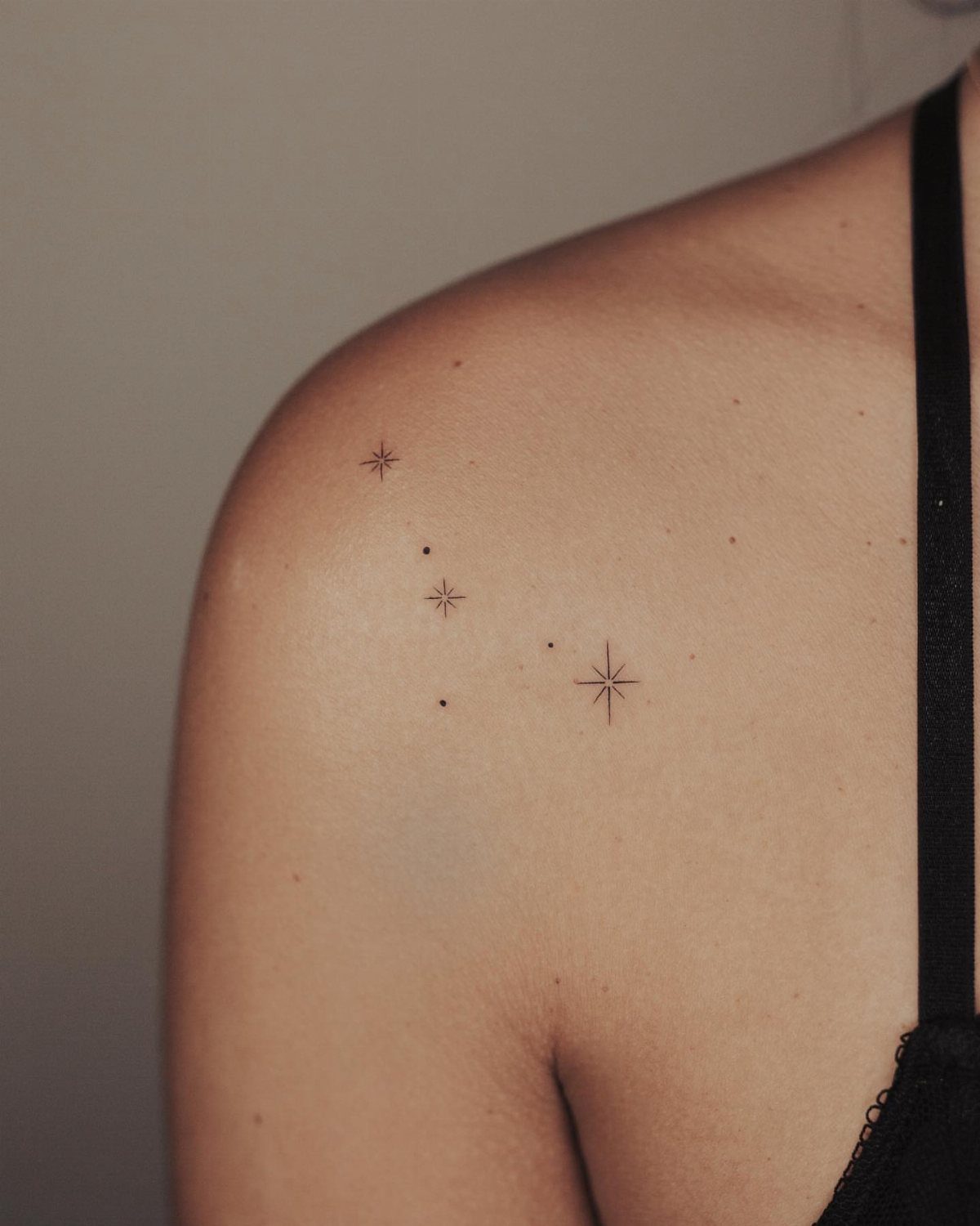 15 Small Tattoo Placement Ideas for Every Style 11 Small black ink star tattoos on a person's shoulder and upper arm.