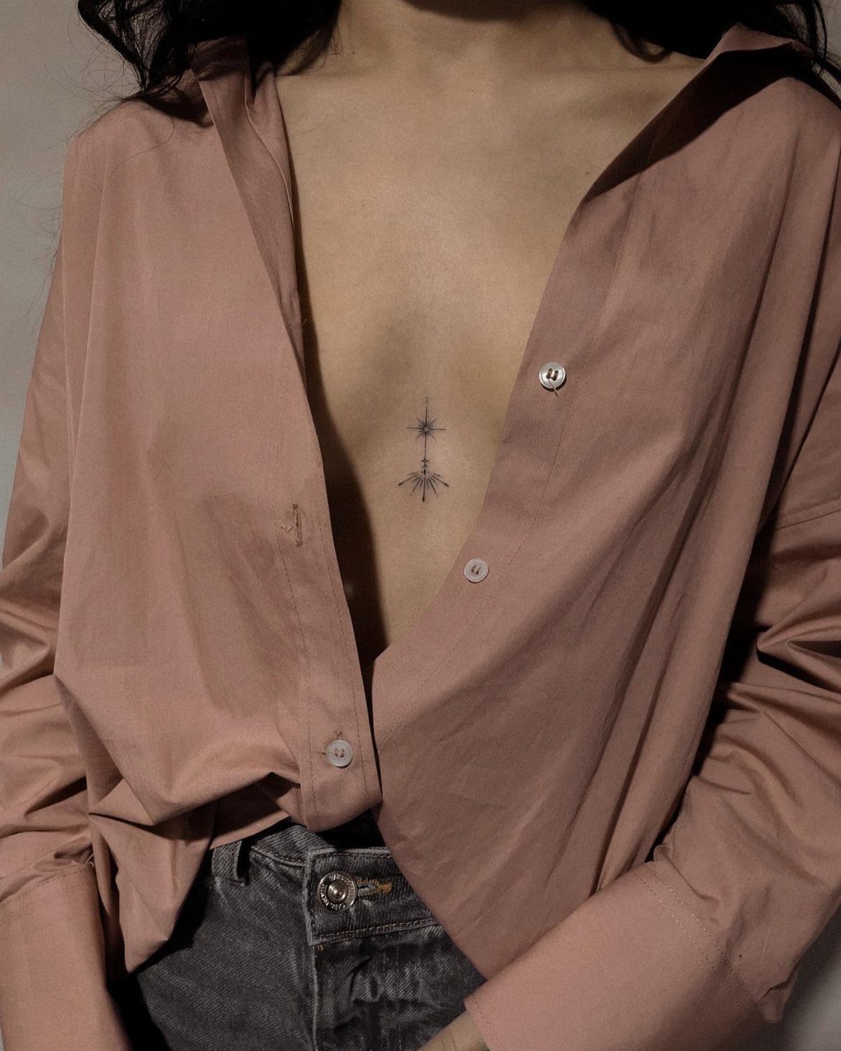 15 Small Tattoo Placement Ideas for Every Style 12 A small star tattoo centered on a person's sternum beneath an open pink shirt.