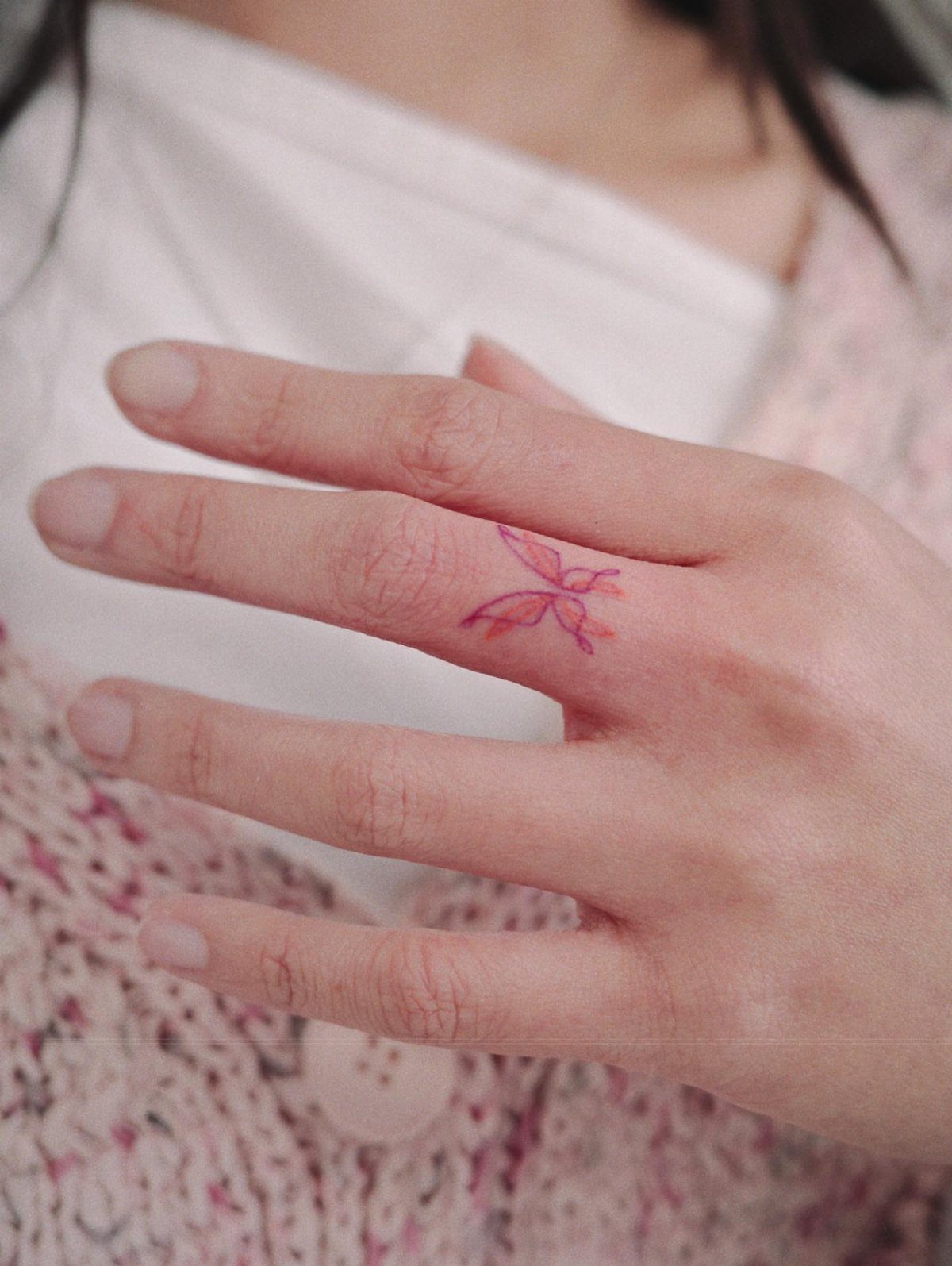15 Small Tattoo Placement Ideas for Every Style 6 A small pink butterfly tattoo on the side of a person's index finger.
