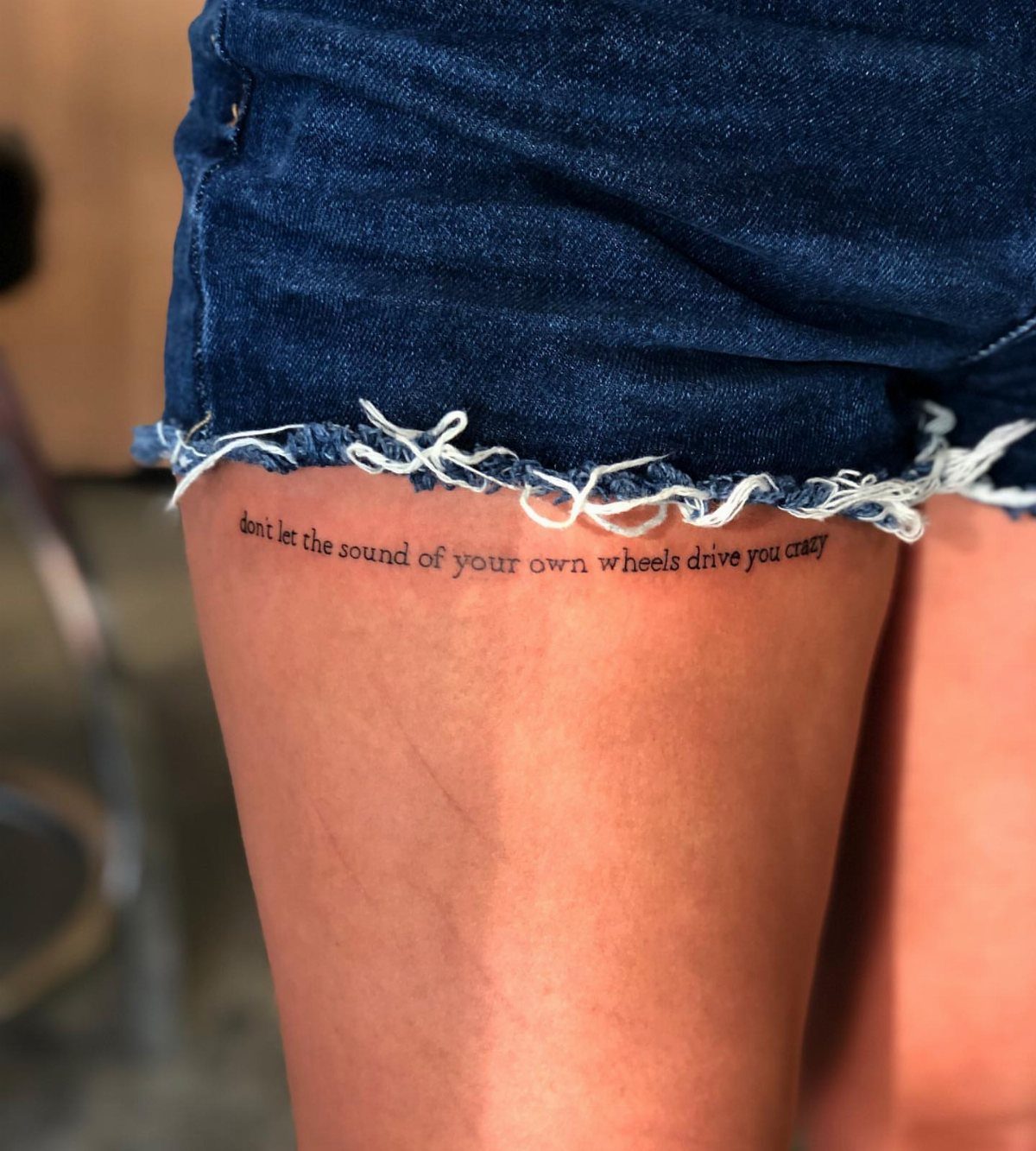 15 Small Tattoo Placement Ideas for Every Style 10 A script tattoo reading 'dont let the sound of your own wheels drive you crazy' on an upper thigh.