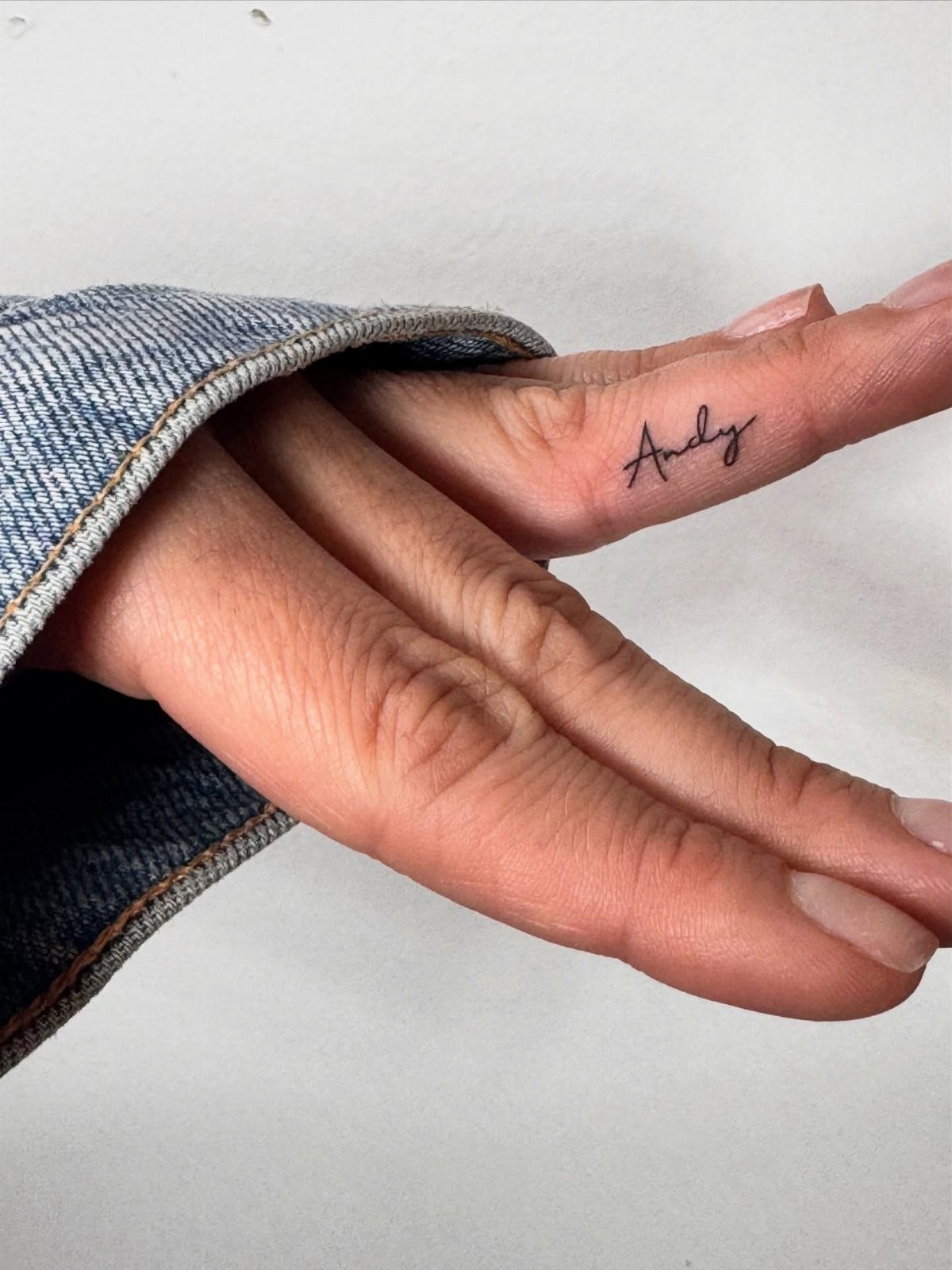 A small cursive tattoo of the name Andy on the side of a person's finger.