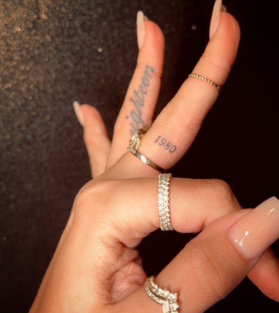 Hand with manicured nails and small tattoos of the word eighteen and the year 1980.