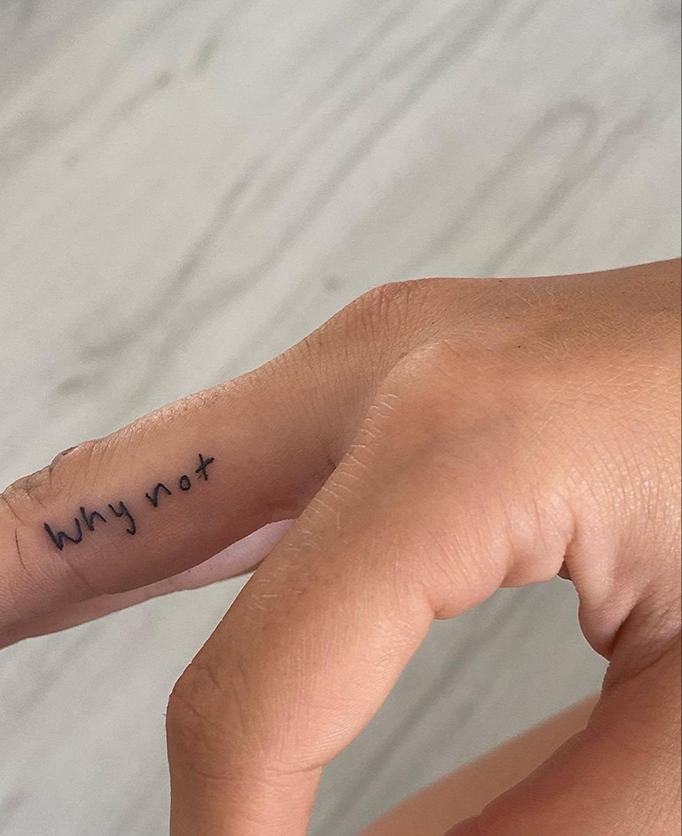 A small black ink tattoo reading why not on the side of a person's finger.