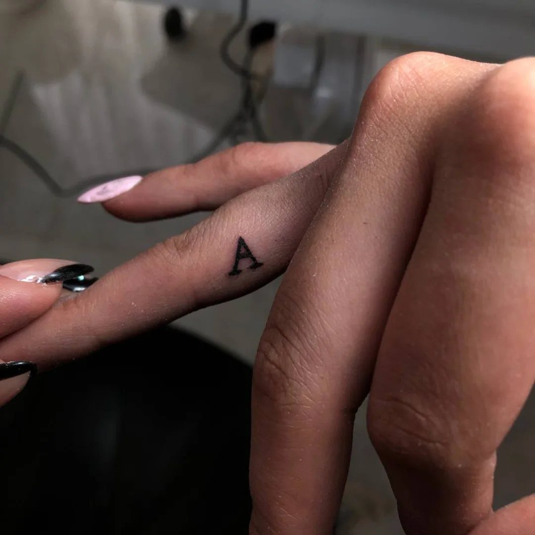A small black letter A tattoo on the side of a person's finger.