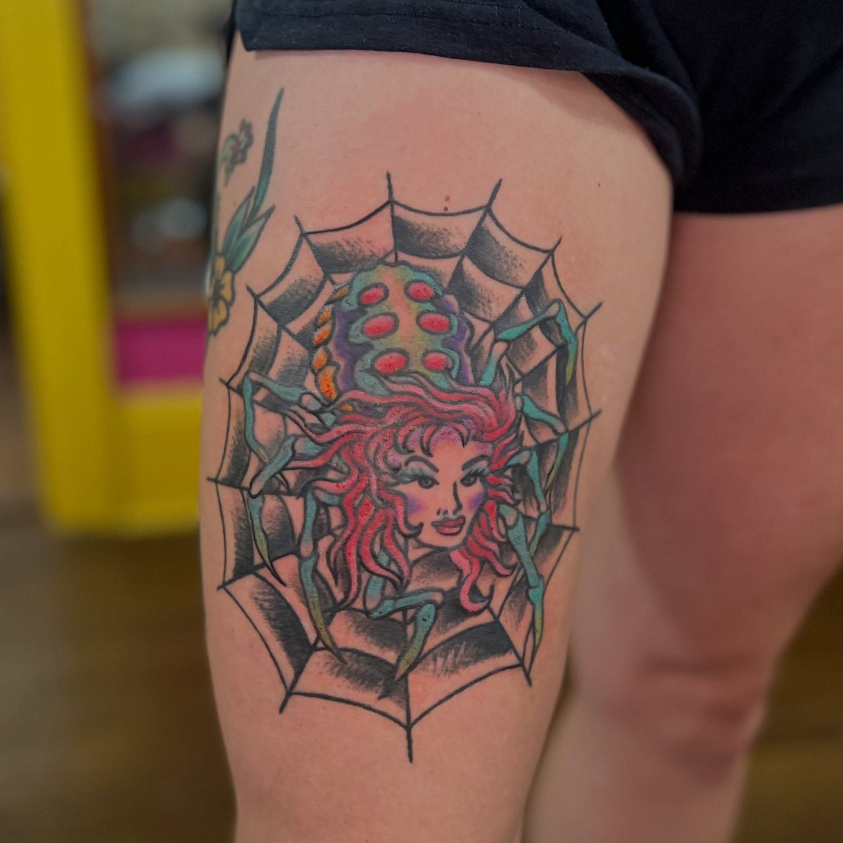 A colorful spider lady tattoo with a woman's face on a person's thigh.