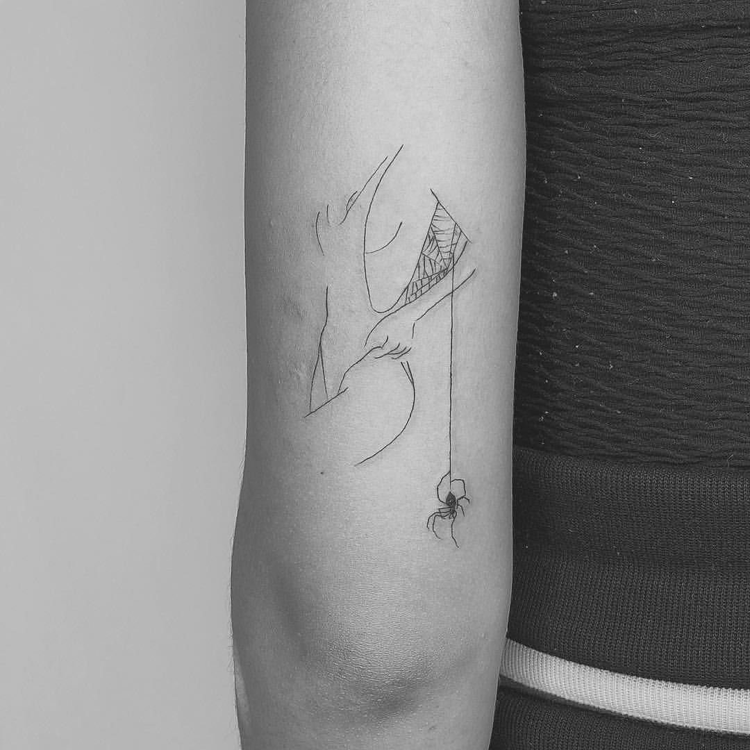 A fine line tattoo on an arm featuring a minimalist woman's face and a small hanging spider.
