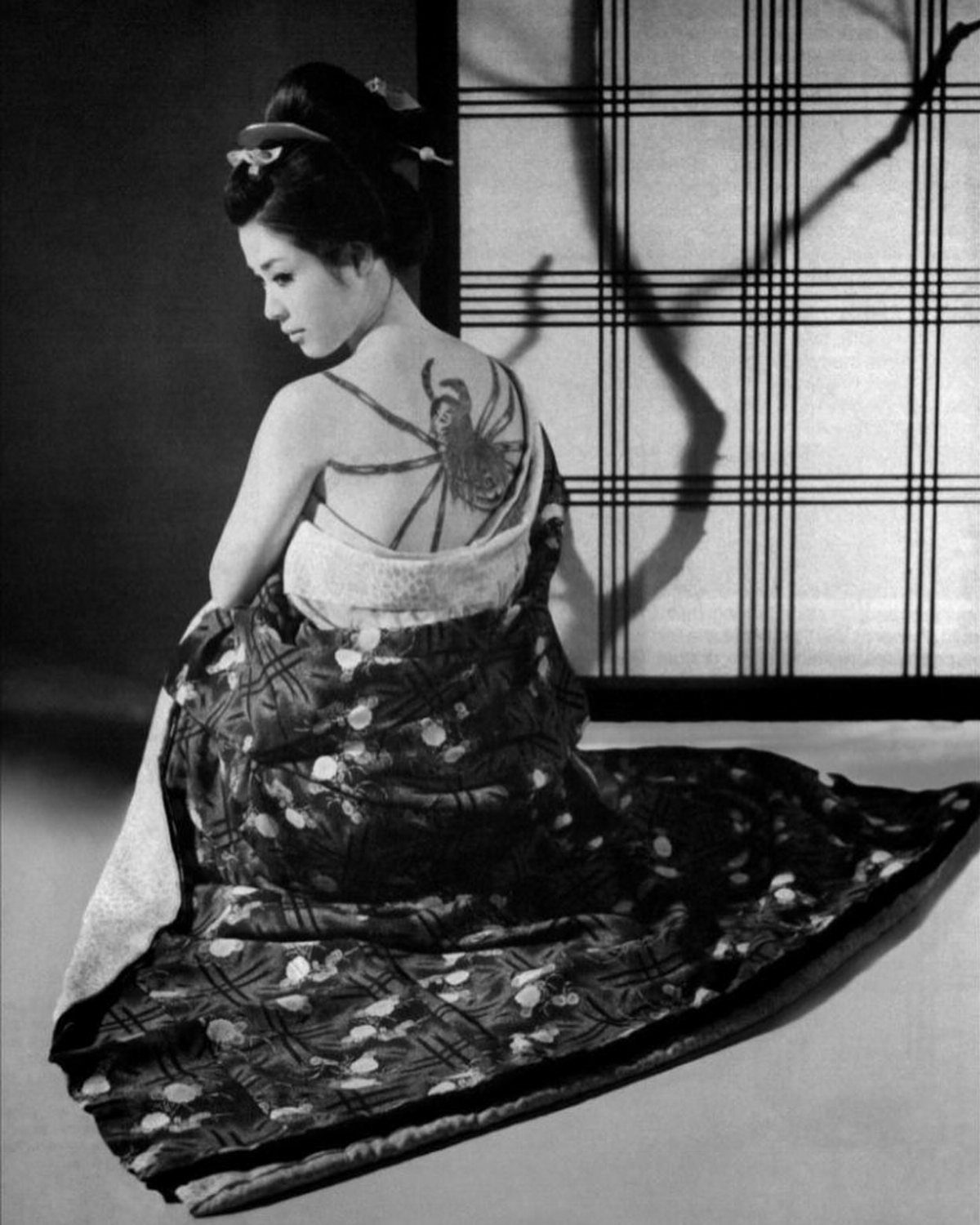 A woman in a kimono showing a large spider tattoo on her upper back.