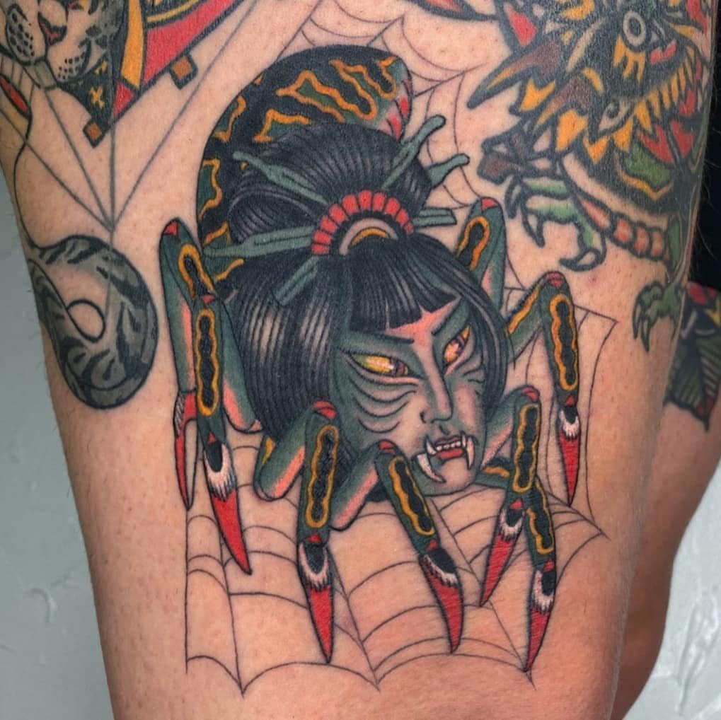 A traditional style tattoo of a spider with a woman's face on a web background.