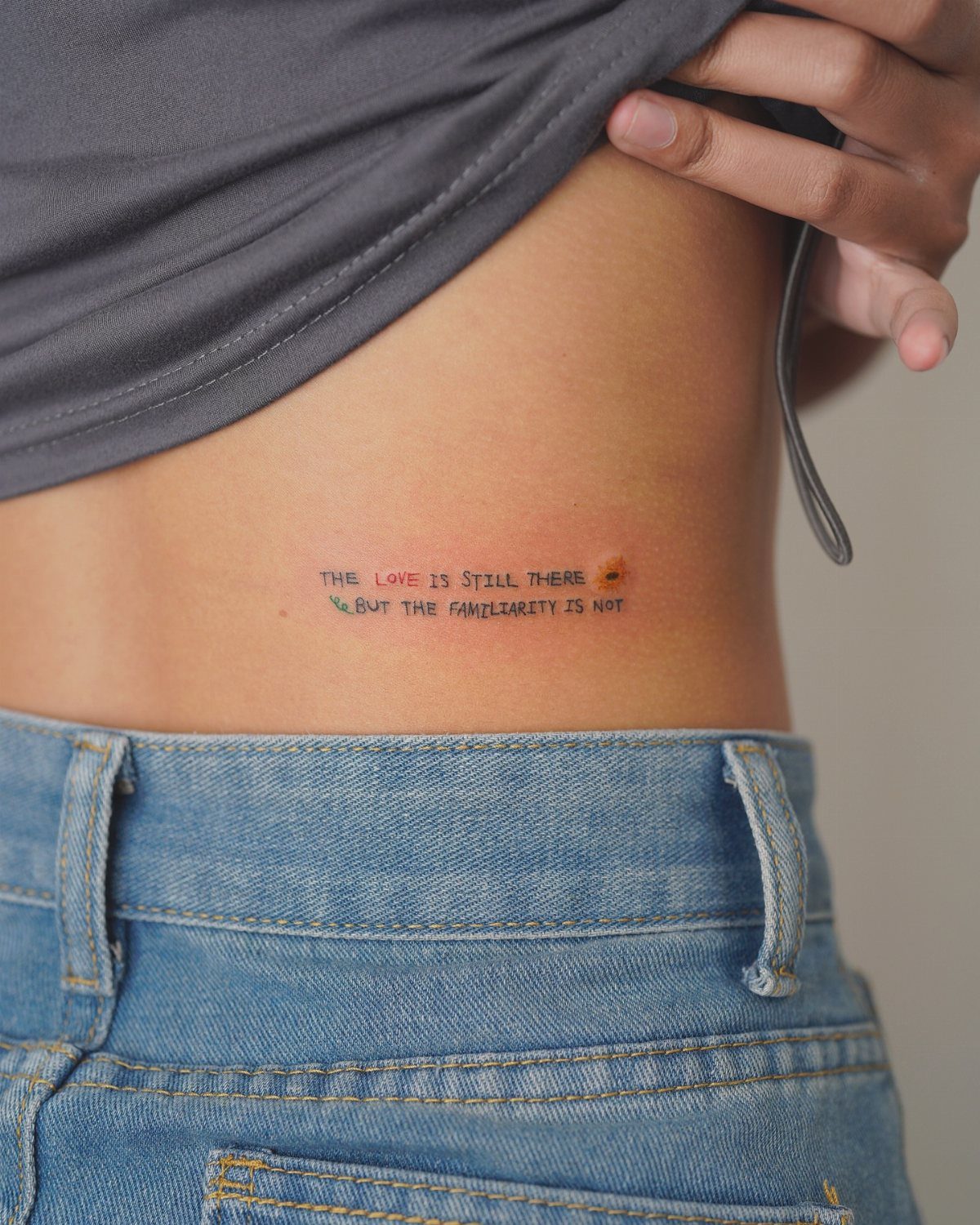 A small text tattoo on a person's lower abdomen above blue denim jeans.