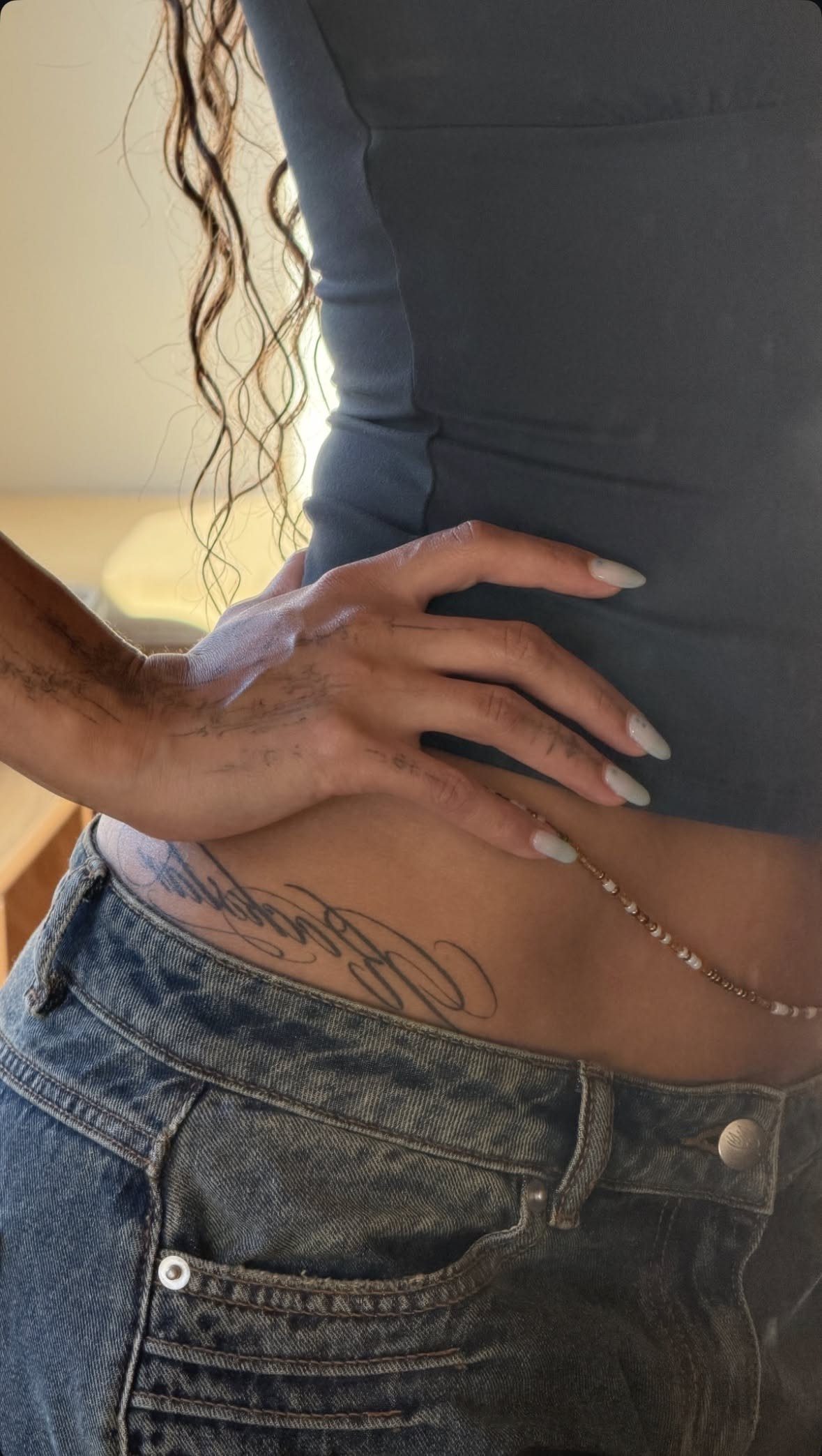 Cursive script tattoo placed along the hip bone of a person wearing denim jeans.