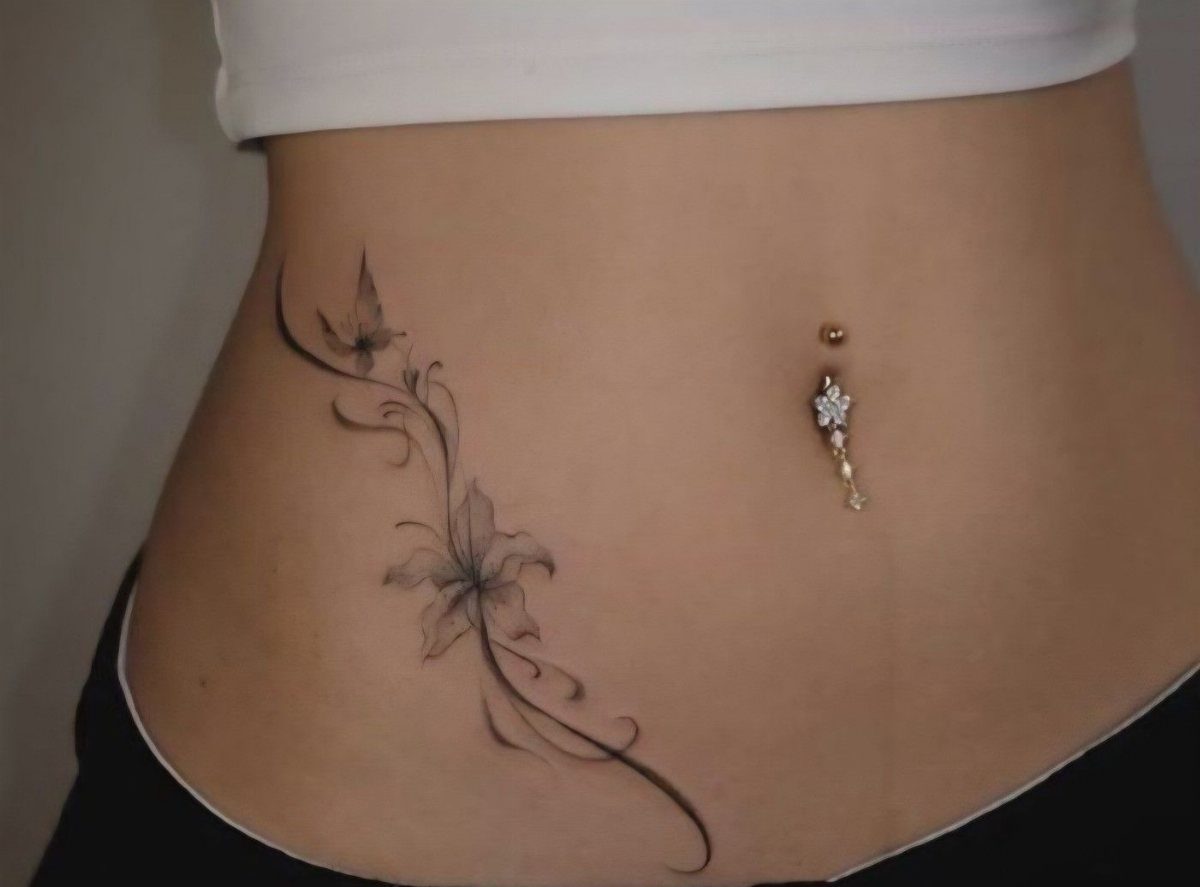 Fine line floral and butterfly tattoo curving along a person's hip and V-line area.