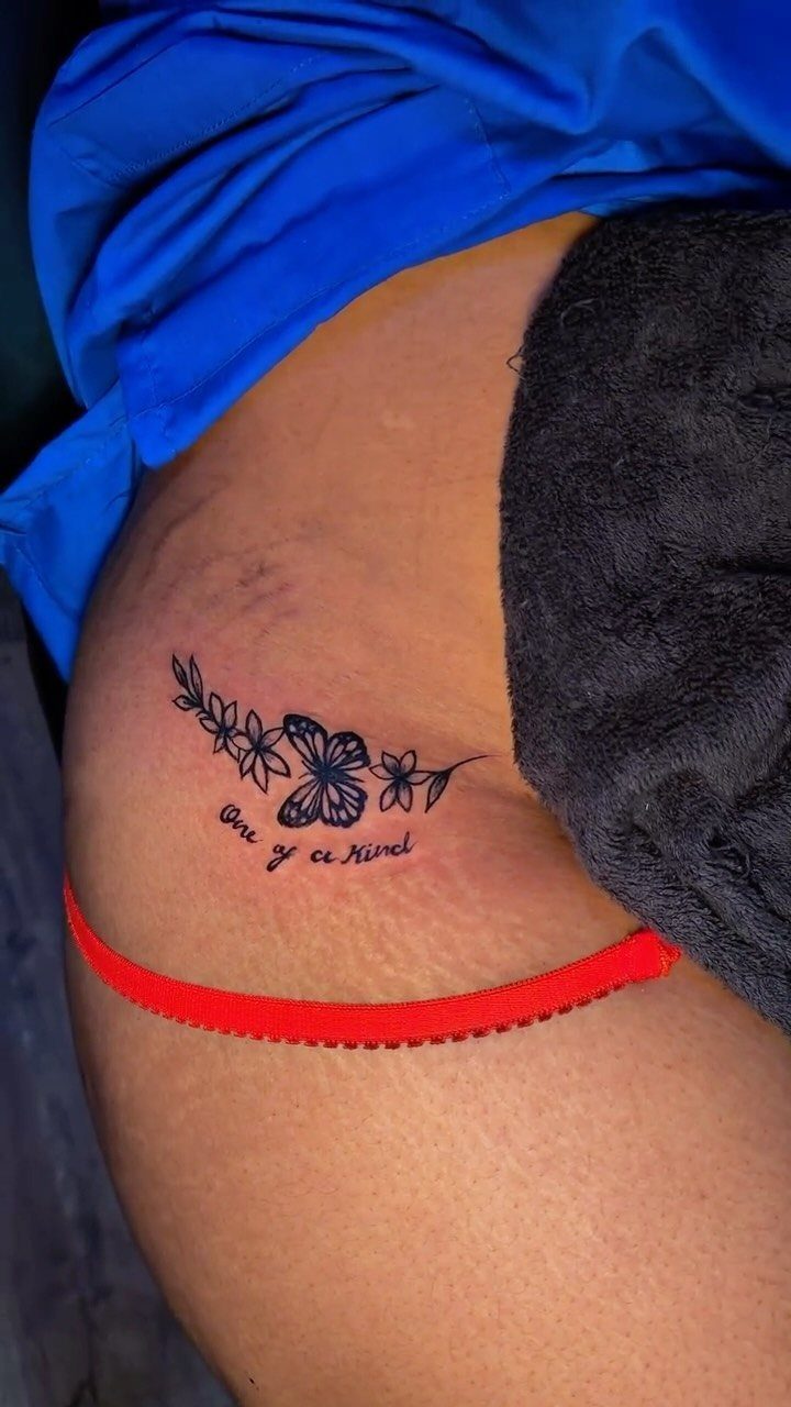 A floral and butterfly tattoo with script text placed on a person's hip near the bikini line.