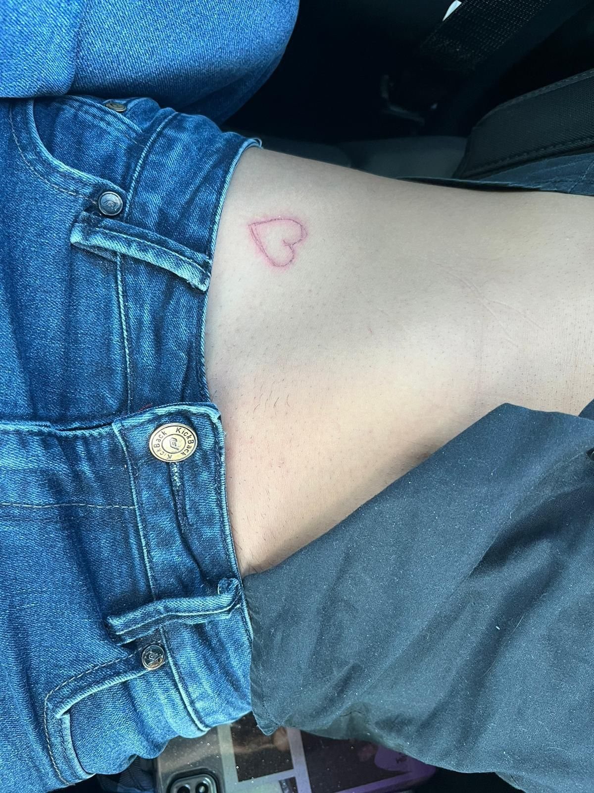 A small red heart outline drawn on a person's hip near blue denim jeans.
