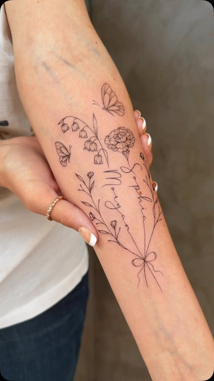 Fine line tattoo of butterflies and flowers with cursive text on a person's forearm.