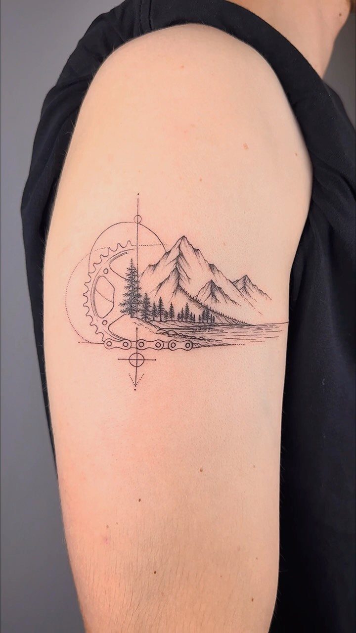 A black ink landscape tattoo on a person's arm featuring mountains, trees, and geometric line art.