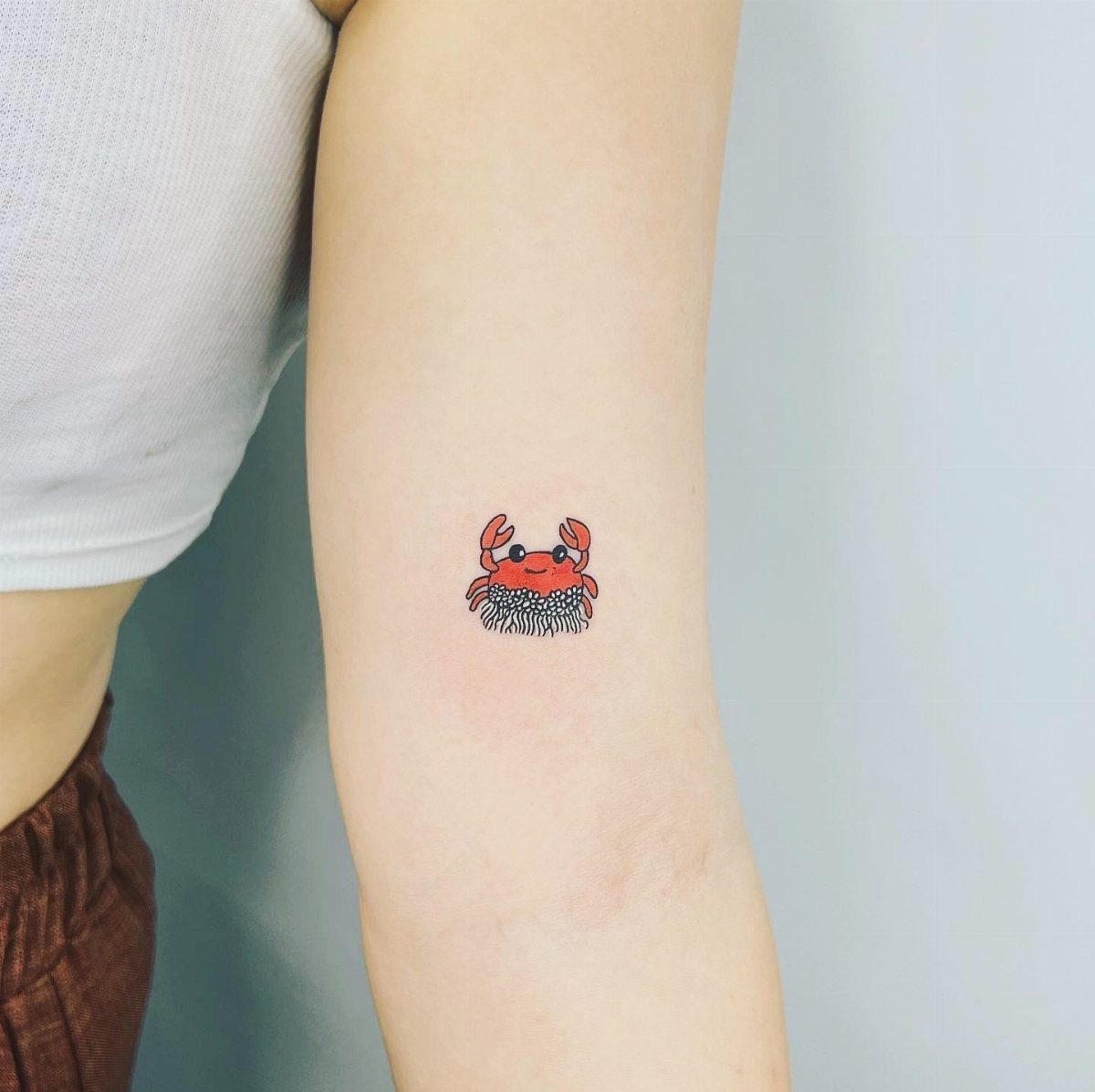 A small red crab tattoo with black outlines on a person's arm.