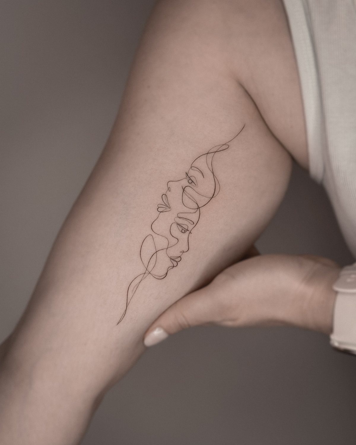 A fine line one line portrait tattoo of two faces on a person's arm.