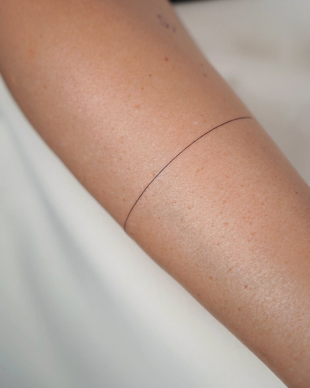 14 Tattoo Style Outline Ideas for Your Next Appointment 12 A thin, minimalist black line tattoo encircling a person's pale arm.
