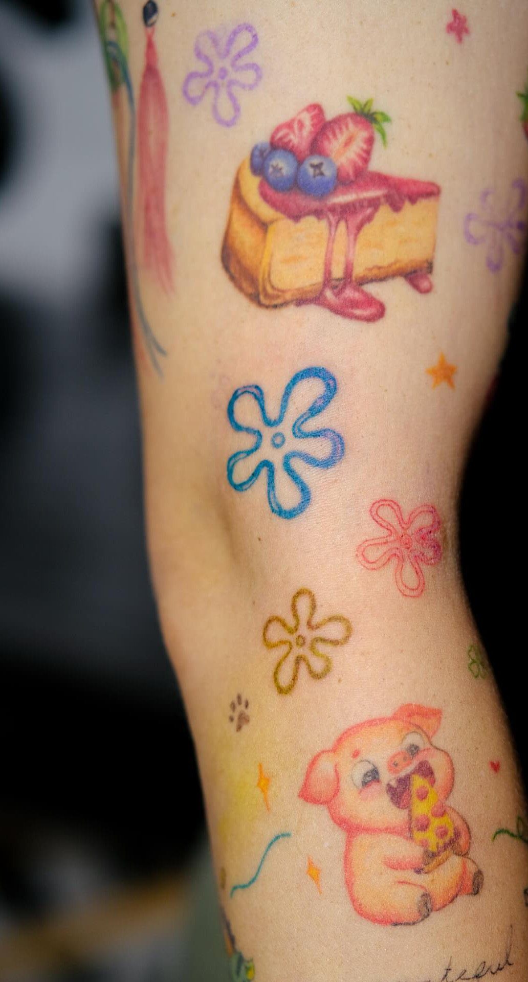 14 Tattoo Style Outline Ideas for Your Next Appointment 7 Colorful tattoos of a strawberry cake, small flowers, and a pig on a person's leg.