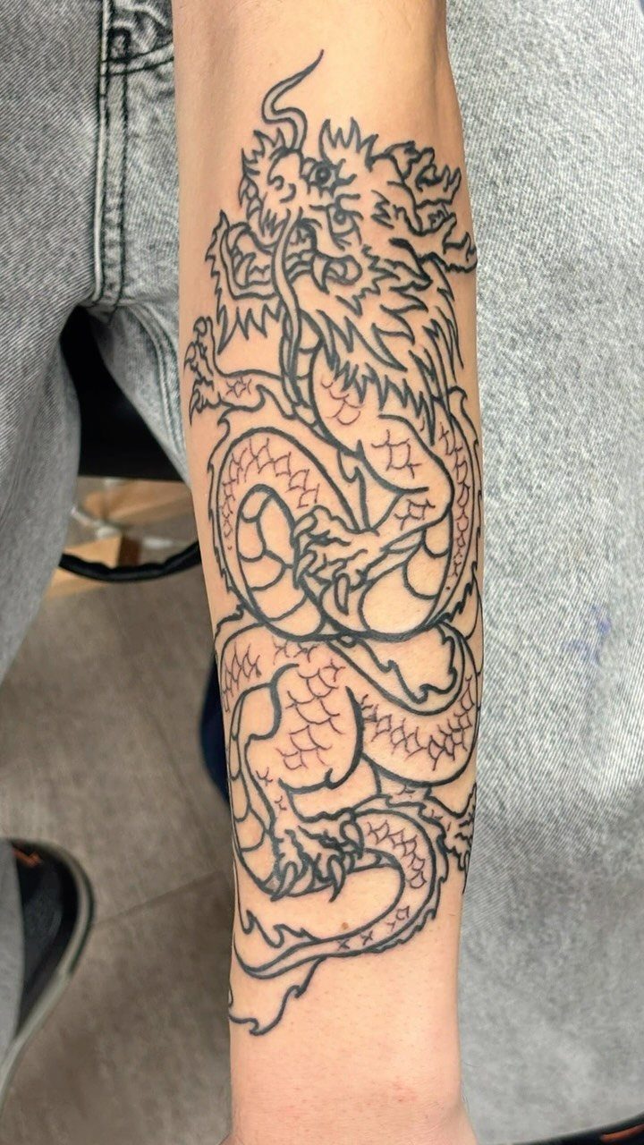 14 Tattoo Style Outline Ideas for Your Next Appointment 6 A detailed black ink dragon outline tattoo on a person's forearm.