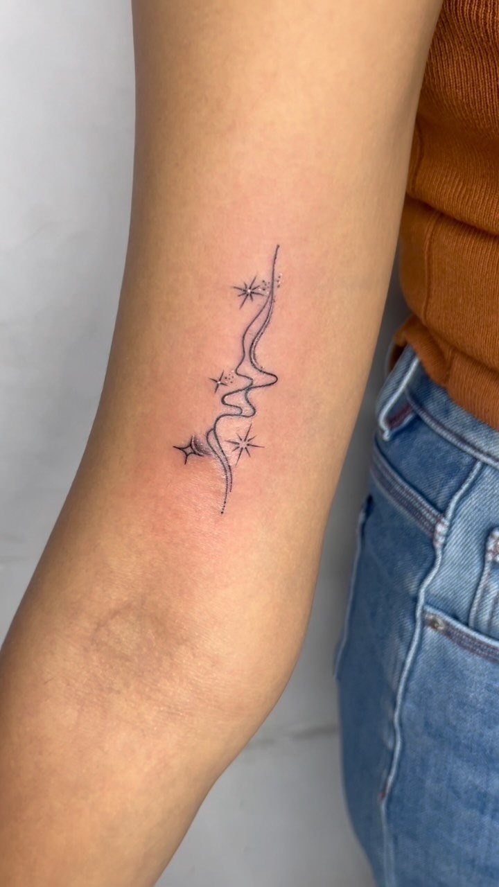 14 Tattoo Style Outline Ideas for Your Next Appointment 11 A minimalist fine-line tattoo of a wavy line and stars on a person's forearm.