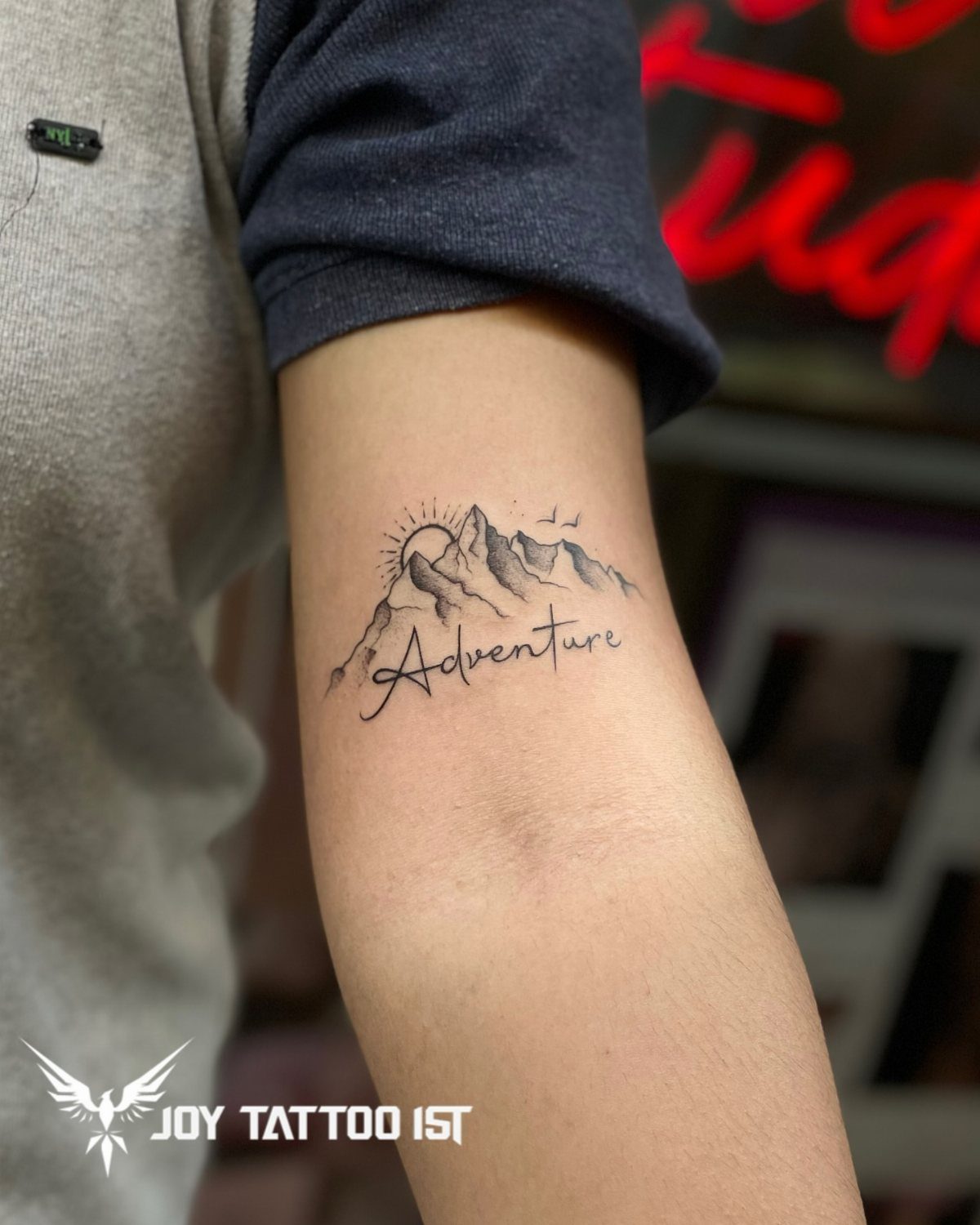 14 Tattoo Style Outline Ideas for Your Next Appointment 2 A mountain range outline tattoo with a sun and the word Adventure on a person's arm.