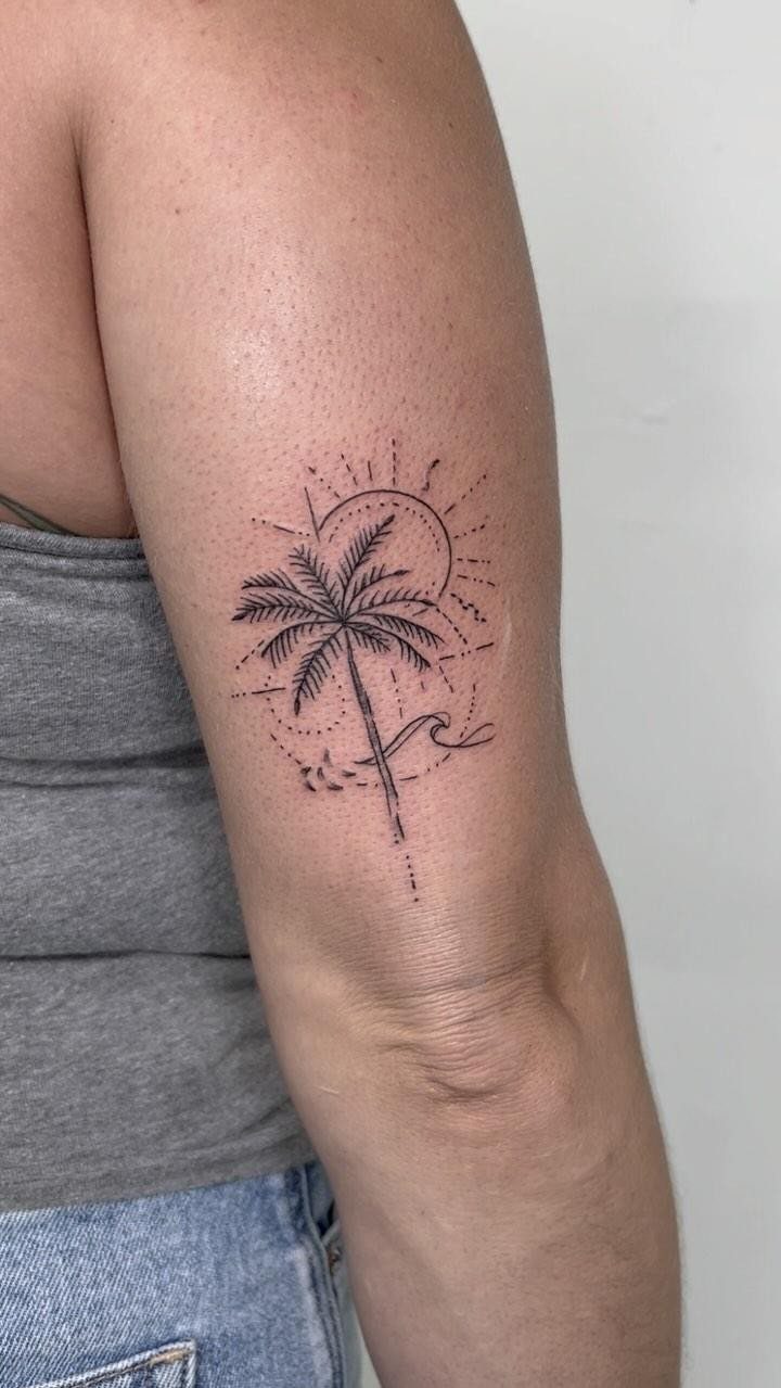 14 Tattoo Style Outline Ideas for Your Next Appointment 8 A fine line black ink tattoo of a palm tree, sun, and wave on an arm.