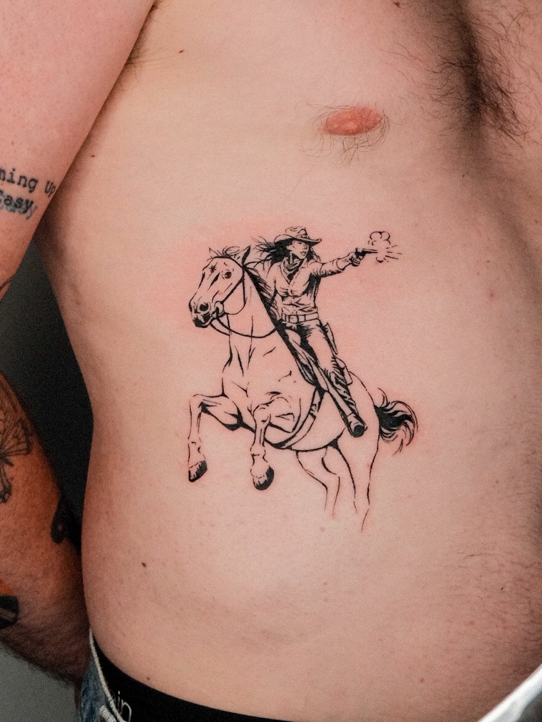 14 Tattoo Style Outline Ideas for Your Next Appointment 13 A black ink tattoo of a cowboy riding a rearing horse on a person's ribs.