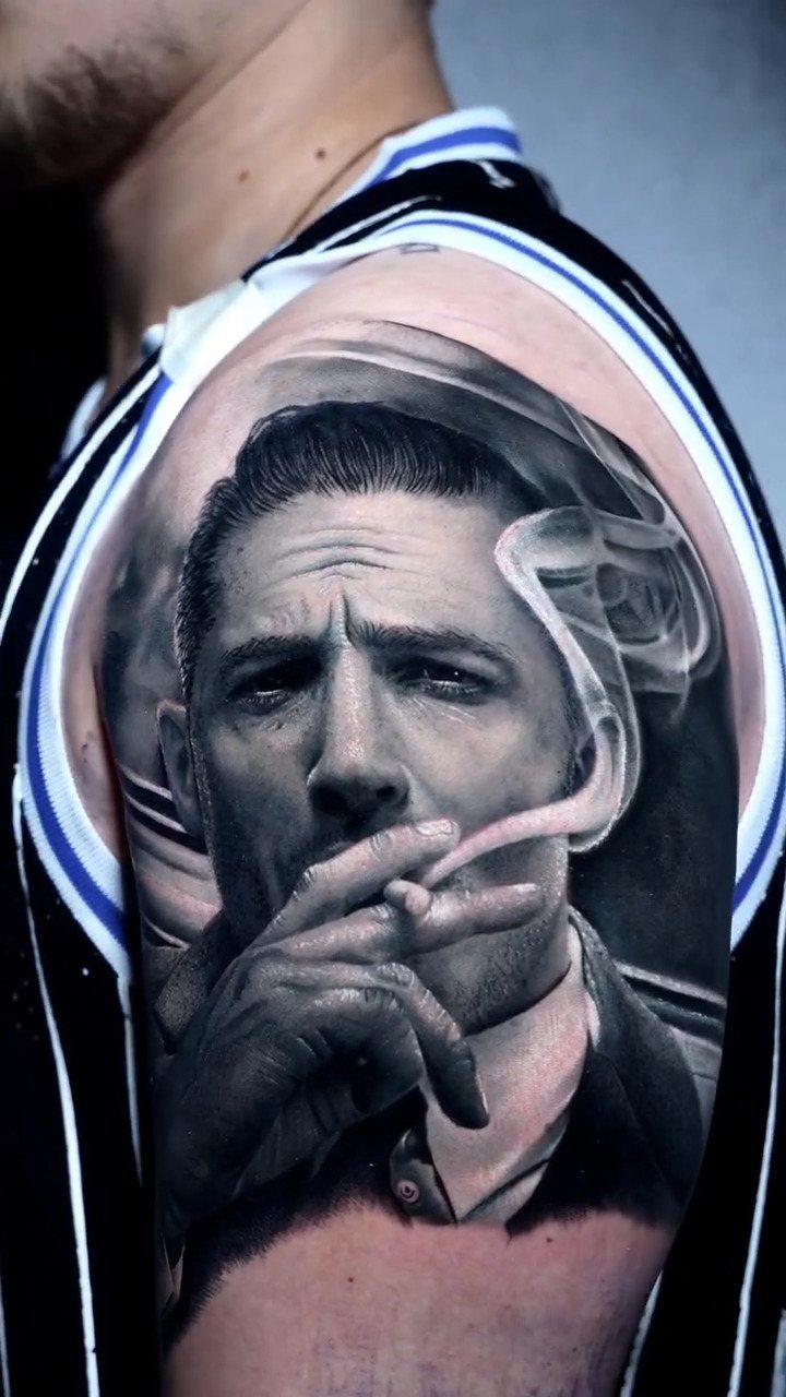 A detailed black and grey realism tattoo of a man smoking on a person's shoulder.