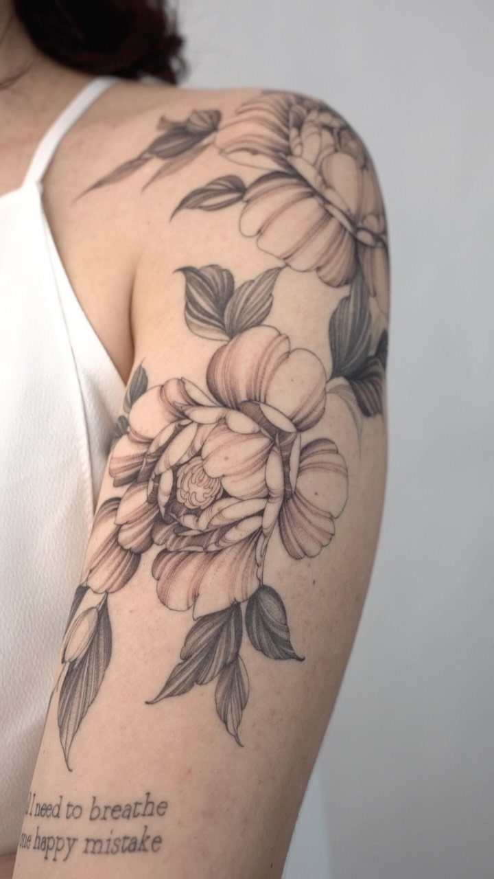 Large black ink peony floral tattoo covering a person's shoulder and upper arm.