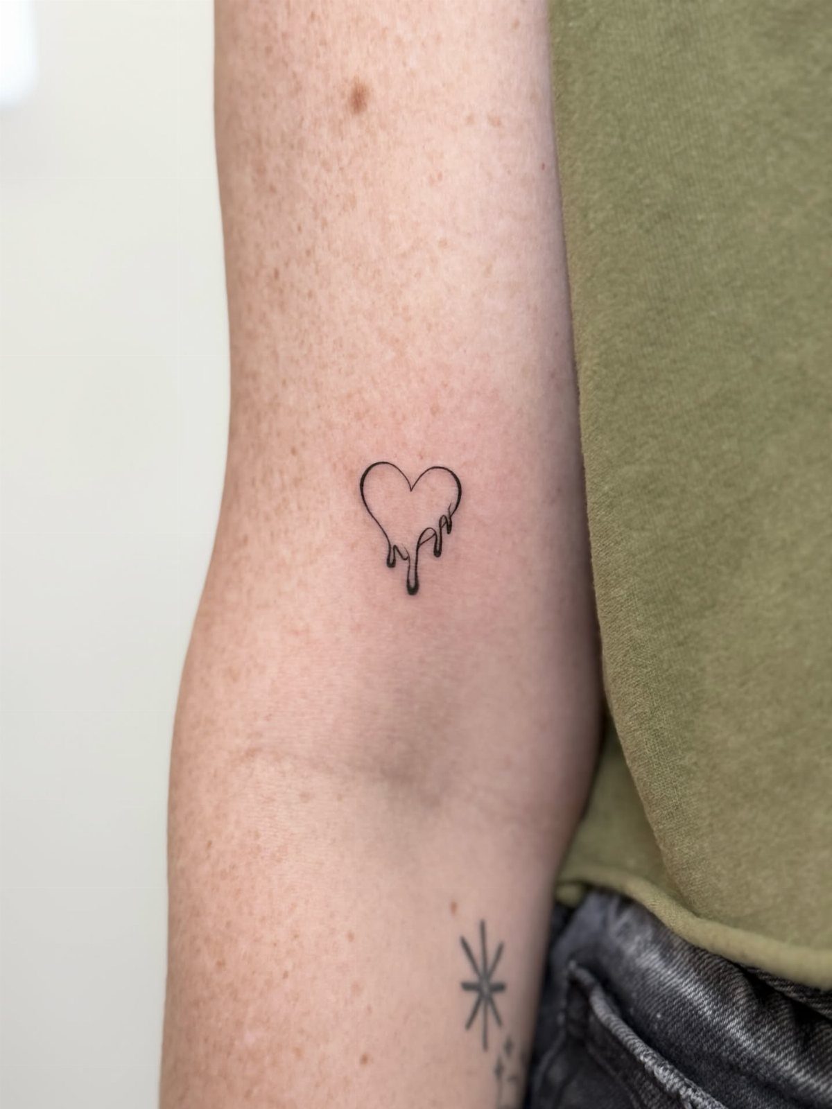 A small black ink tattoo of a dripping heart on a person's arm.