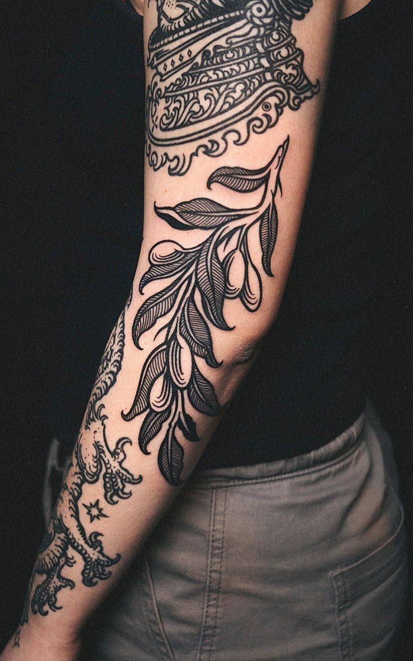 Black ink woodcut style tattoos on a person's arm featuring leaves and ornate patterns.