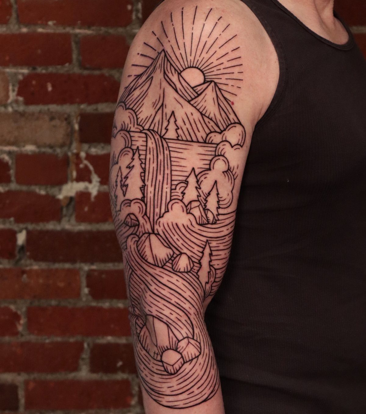 A woodcut style landscape tattoo on an arm showing mountains, trees, and a sun.