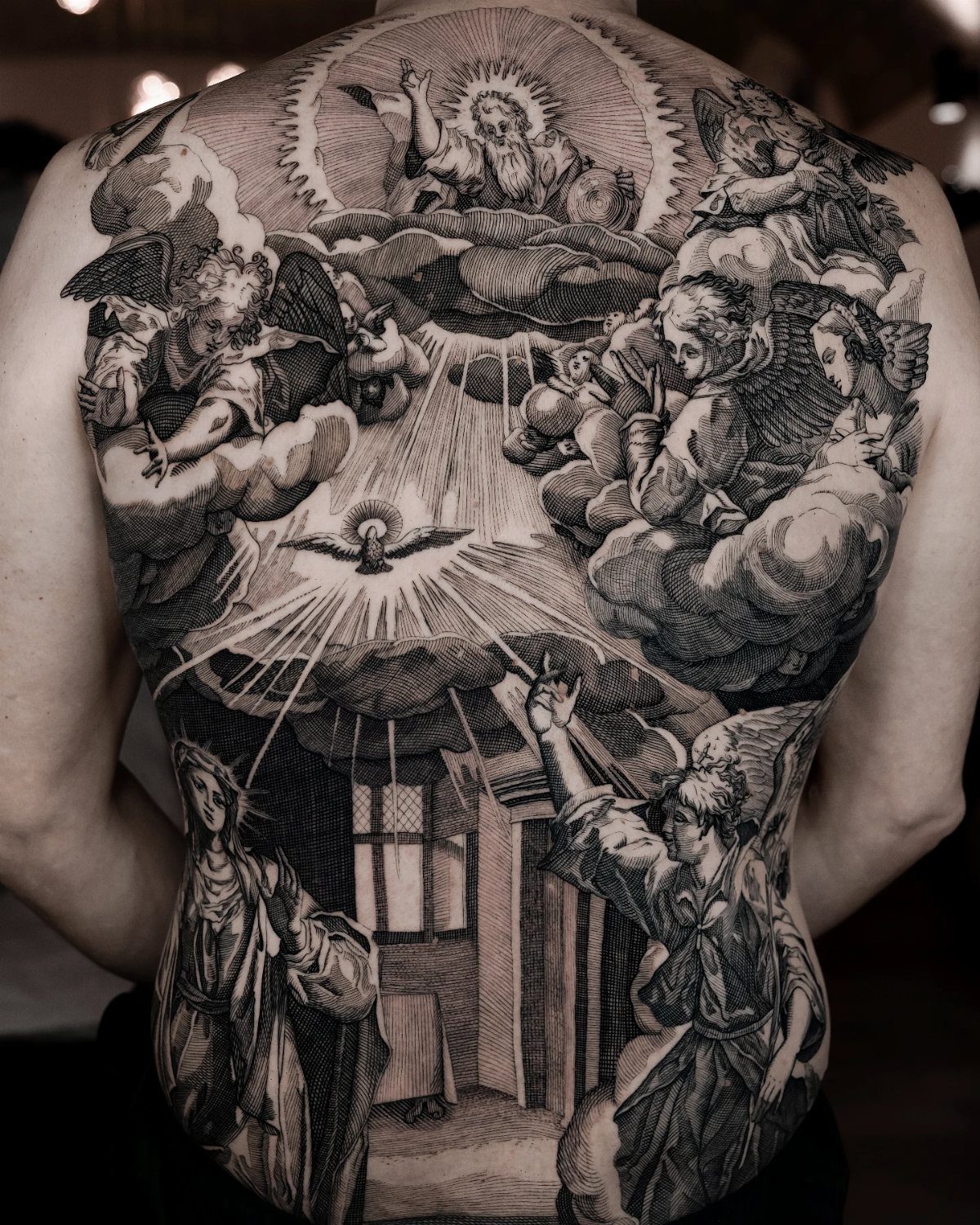 A large back tattoo depicting religious figures and angels in a detailed woodcut engraving style.