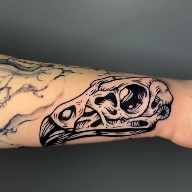 A black ink woodcut style bird skull tattoo on a person's forearm.