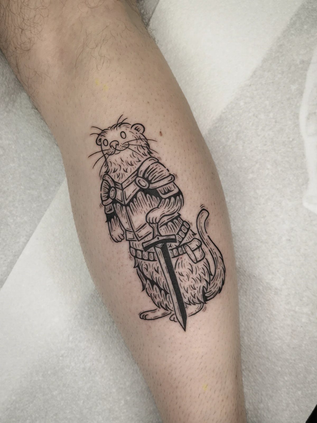A woodcut style tattoo of an armored animal holding a sword on a person's leg.