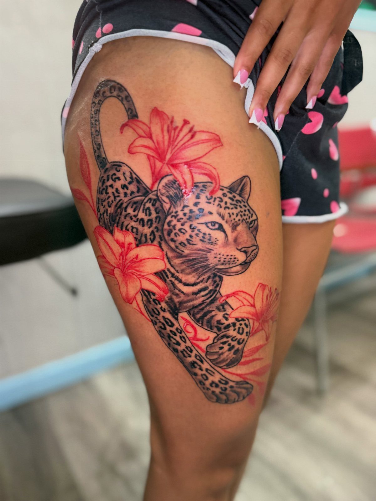 A leopard tattoo with red lilies on a person's thigh.
