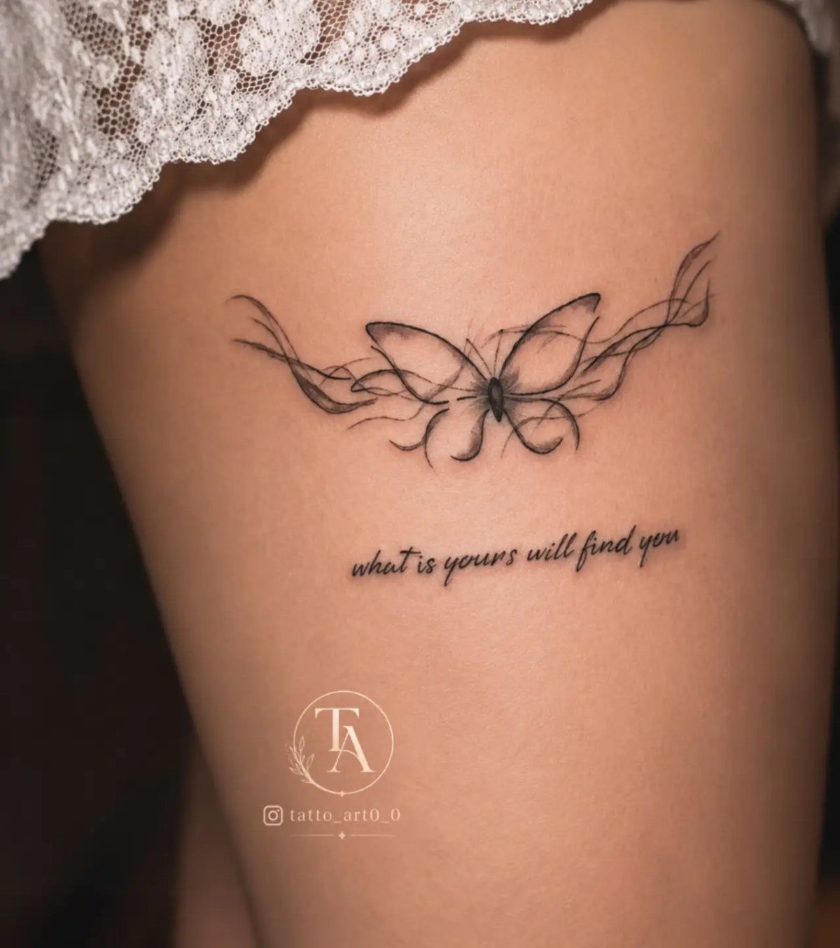 A delicate black ink butterfly tattoo with flowing lines and script text on a thigh.
