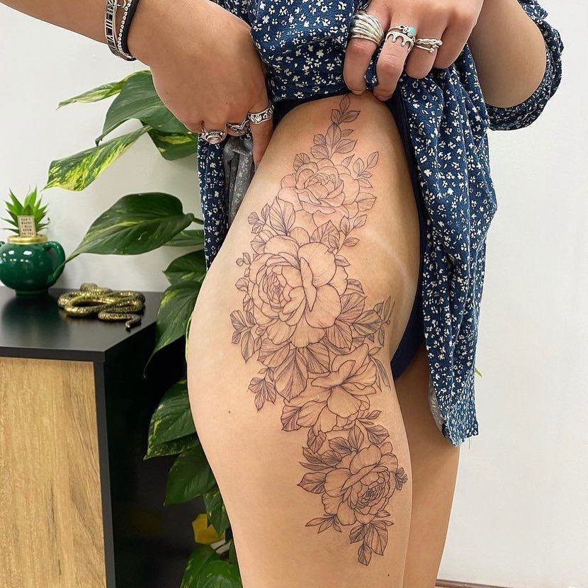 A large black ink rose and floral tattoo on a person's upper thigh.