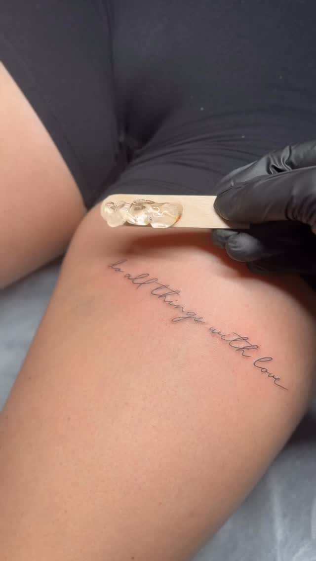 A script tattoo on a person's thigh reading do all things with love.