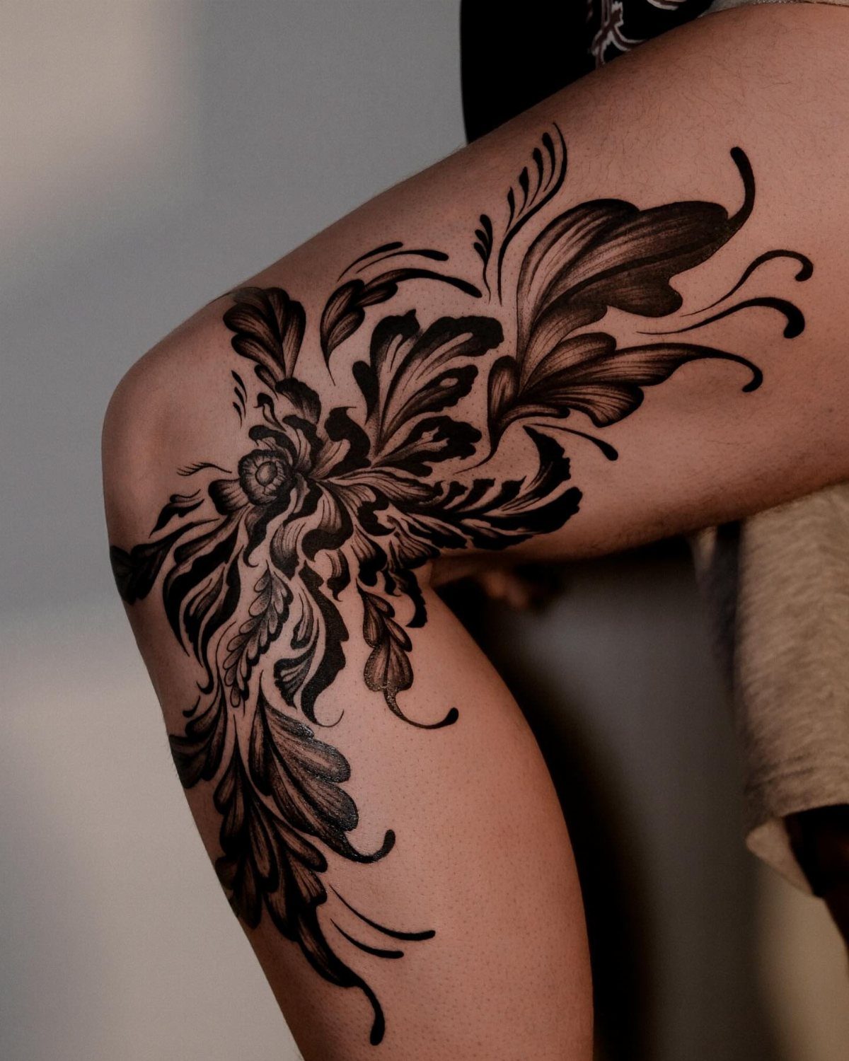 Large blackwork floral tattoo covering a person's thigh and extending down towards the knee.