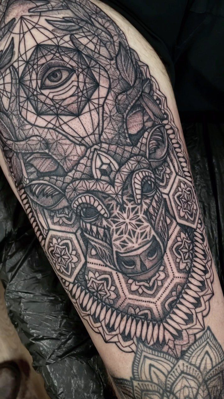 A large black ink geometric tattoo with mandala patterns on a person's thigh.