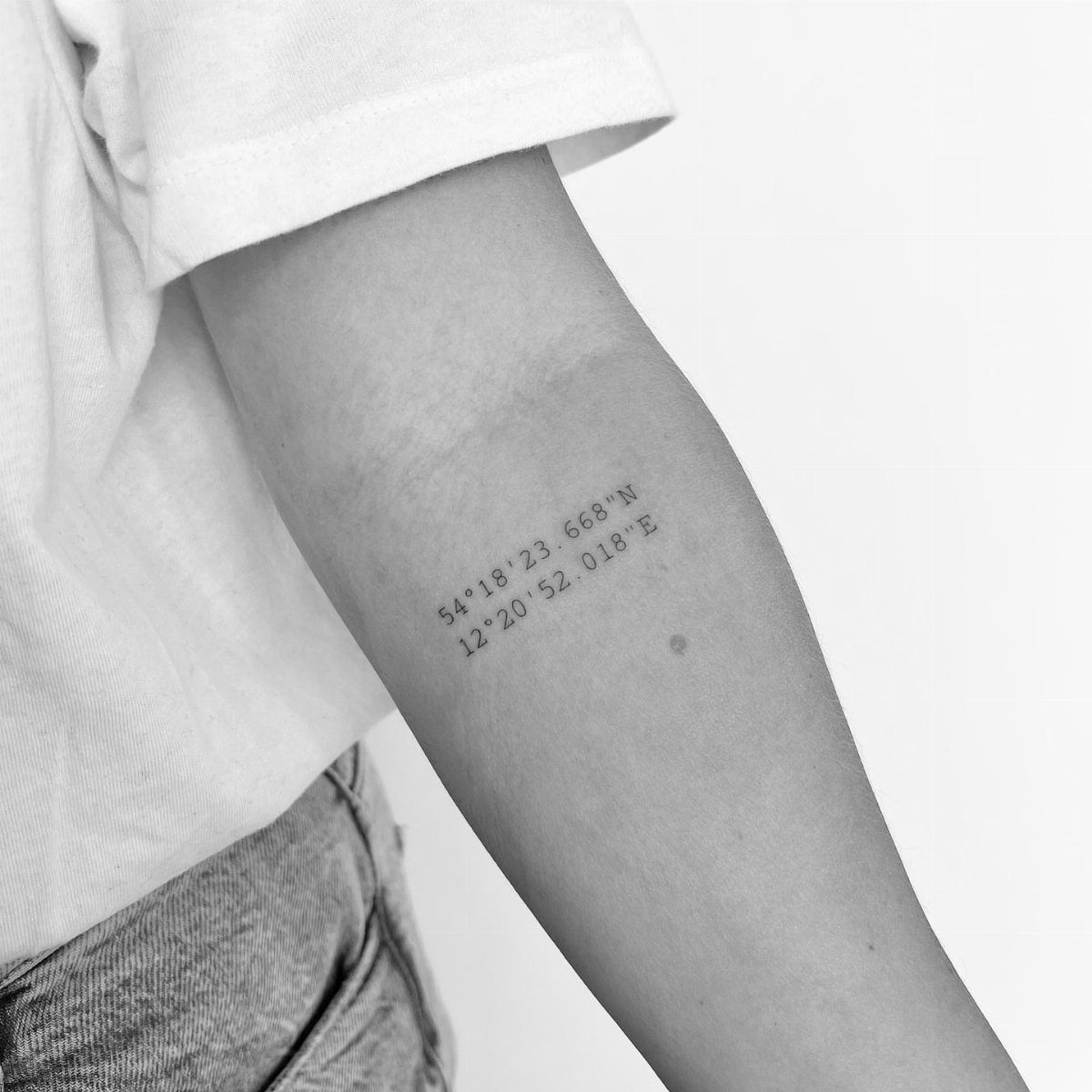 8 Tiny Travel Tattoo Ideas for Your Next Piece of Ink 1 A small tattoo of geographic coordinates on a person's forearm in black and white.