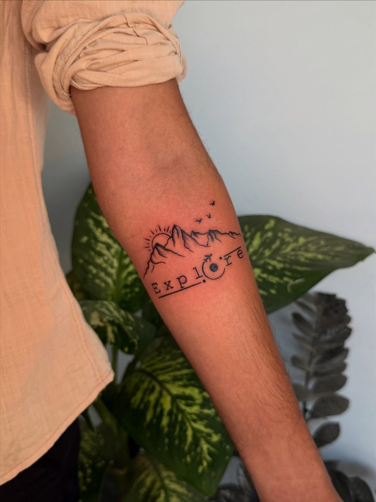 8 Tiny Travel Tattoo Ideas for Your Next Piece of Ink 8 A small black ink tattoo of mountains and the word Explore on a person's forearm.